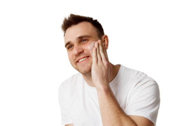 Kısa esmer saçlı, yanağına nemlendirilmiş yüz bakımı uygulayan ve beyaz stüdyo geçmişine bakan çekici bir genç. Doğal güzellik kavramı, spa tedavileri, kozmetoloji.