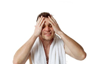 Sabah rutini. Omuzlarında havlu olan bir adamın portresi beyaz stüdyo arka planına su sıçratarak yüzünü yıkıyor. Doğal güzellik kavramı, spa tedavileri, erkeksi, kozmetoloji.