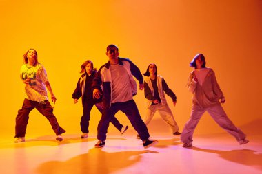 Sokak kıyafetleri içinde hip-hop yapan bir grup dansçı rengarenk stüdyo arka planına karşı neon ışıkta dans ediyorlar. Hobi, spor, moda ve tarz kavramı, eylem, gençlik kültürü, müzik ve dans.