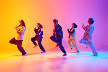 Dinamik hareketli dansçılar, modern hip-hop dans stillerini neon ışıkta, rengarenk stüdyo arkaplanına karşı gösteriyorlar. Hobi, spor, moda, aksiyon, gençlik kültürü, müzik ve dans kavramı.
