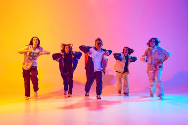 Enerjik dans ekibi, renkli stüdyonun arka planına karşı neon ışıkta çağdaş dans hareketleri sergiliyor. Hobi, spor, moda ve tarz kavramı, eylem, gençlik kültürü, müzik ve dans.