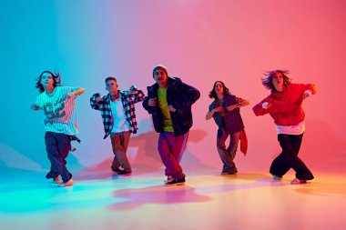 Dans topluluğu, neon ışıkta, rengarenk stüdyo arkaplanına karşı enerjik bir şekilde hareket ediyor. Hareket var. Hobi, spor, moda ve tarz kavramı, eylem, gençlik kültürü, müzik ve dans.