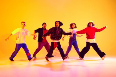 Sokak kıyafetleri içinde hip-hop yapan bir grup dansçı rengarenk stüdyo arka planına karşı neon ışıkta dans ediyorlar. Hobi, spor, moda ve tarz kavramı, eylem, gençlik kültürü, müzik ve dans.