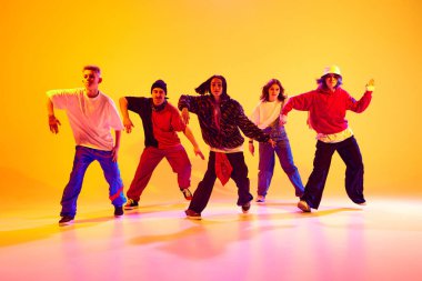 Dinamik hareketli dansçılar, modern hip-hop dans stillerini neon ışıkta, rengarenk stüdyo arkaplanına karşı gösteriyorlar. Hobi, spor, moda, aksiyon, gençlik kültürü, müzik ve dans kavramı.