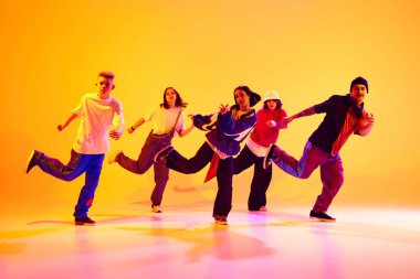 Modern dans ekibi senkronize hareket halinde, rengarenk stüdyo arka planına karşı neon ışıkta hip-hop yapıyor. Hobi, spor, moda ve tarz kavramı, eylem, gençlik kültürü, müzik ve dans.