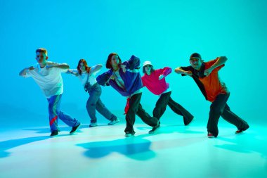 Retro giyimli bir grup yetenekli dansçı, gradyan stüdyo arka planına karşı neon ışığı altında koreografi çalışması yapıyor. Hobi, spor, moda, aksiyon, gençlik kültürü, müzik ve dans kavramı.