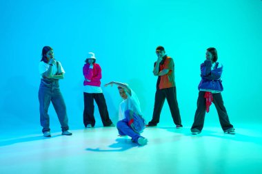 Dans savaşları. Genç adam dans takımıyla neon ışıkta rengarenk stüdyo arkaplanına karşı breakdance hareketleri yapıyor. Hobi, spor, moda, gençlik kültürü, müzik ve dans kavramı.