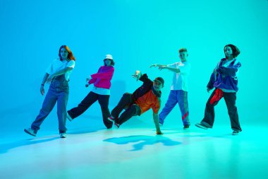 Sokak stili dansçılardan oluşan bir grup neon ışıkta rengarenk stüdyo arkaplanına karşı enerjik bir şekilde senkronize hareket ediyor. Hobi, spor, moda ve tarz kavramı, eylem, gençlik kültürü, müzik ve dans.