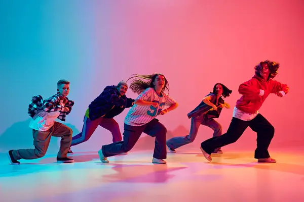 stock image Casually dressed teenagers perform forward-moving dance sequence in neon light against gradient studio background. Concept of hobby, sport, fashion and style, action, youth culture, music and dance.