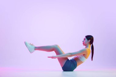 Genç bayan sporcu, karnın kaslarını statik pozda eğitiyor. Neon ışıkta, gradyan stüdyo arka planına karşı. Spor ve eğlence anlayışı, hareket, kişisel bakım, eylem, enerji. Ad