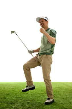 Eski moda kıyafetli ve şapkalı neşeli golfçü, mükemmel golü kutluyor. Yumruğunu kaldırmış ve golf sopası beyaz arka plana karşı yeşil sahada duruyor. Spor anlayışı, lüks oyunlar, aktif yaşam tarzı. Ad