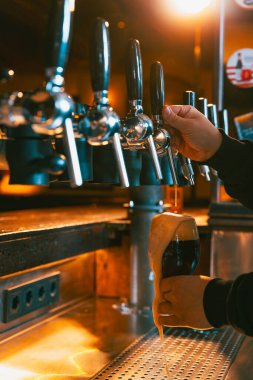 Marangoz, bira, soğuk, köpüklü siyah bira geleneksel bardaki barmen tarafından bardağa döküldü. Musluktan bira servisi. Alkol içecekleri, gece hayatı, parti, festivaller, Ekim Festivali. Ad