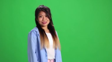 Kendine güvenen genç Asyalı bayan, günlük kıyafetli öğrenci canlı yeşil stüdyo geçmişiyle kameraya bakıyor. Uzayı kopyala İnsan duyguları kavramı, kendini ifade etme, moda, tarz. Ad