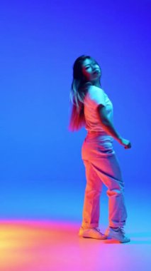 Neşeli genç Asyalı kadın gündelik kıyafetlerle dans ediyor mavi ışıkta arka planda el kaldırıyor. İnsan duyguları kavramı, kendini ifade etme, dans ve müzik, eğlence ve neşe. Ad