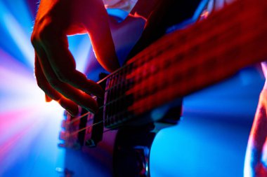 Gitaristlerin elleri, bulanık arka planda dinamik sahne aydınlatmalı elektro gitar tellerini koparıyor. Rock ve klasik müzik kavramı, hobi ve iş, enerji, müzik festivalleri, konserler. Ad