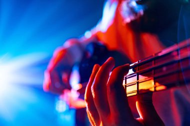 Basçıların elleri yeni parçaların melodik akortlarını çalarken arka planda renkli bir konser ışığı parlıyor. Rock ve klasik müzik kavramı, hobi ve iş, enerji, müzik festivalleri, konserler. Ad