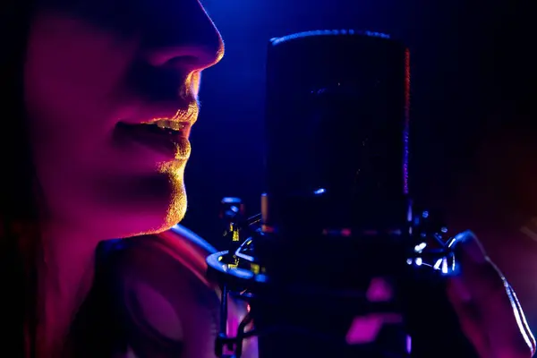 Profile view of woman, professional artistic vocalist singing, with microphone and intense purple stage light. Concept of art, work and hobby, music festivals, self expression, concert. Ad