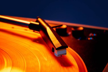 Retro vinil oynatıcının makro fotoğrafı, vinil dalgaların yüzeyi sıcak turuncu ışık altında fonograf iğnesi. Sanat anlayışı, retro müzik, disko, klasik, nostalji, eski moda. Ad