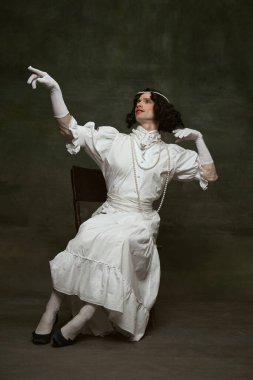 Zarif, eski moda bir elbise giyen ve klasik stüdyo arka planına karşı derin düşüncelere sahip bir başlık takmış bir adam. Kendini ifade etme kavramı, dönemin karşılaştırmaları, özgürlük, insan hakları.