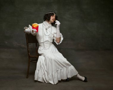 Eski moda elbiseli bir adamın portresi ve klasik stüdyo arka planıyla modern restorandan patates kızartması yemek. Kendini ifade etme kavramı, dönemin karşılaştırmaları, özgürlük, insan hakları.