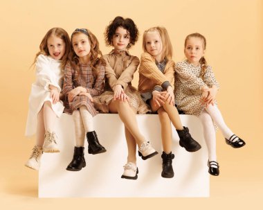 Beş küçük kız grubu şık kıyafetler içinde bej renkli stüdyo geçmişine karşı neşeli ifadelerle birlikte oturuyorlar. Moda ve tarz kavramı, güzellik, Kara Cuma, satış sezonu, alışveriş.