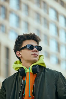 Kendine güvenen genç adam neon akımı benimsiyor. Aşırı büyük giyimi, sokak kıyafetlerinin eklektik birleşimini ve çağdaş modayı yansıtıyor. Sokak kavramı, şehir tarzı, yaşam tarzı, Z jenerasyonu, kendini ifade etme