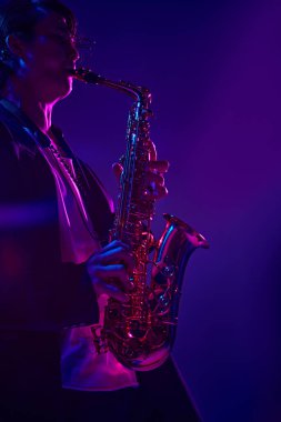 Koyu takım elbiseli genç çekici bir adamın portresi. Stüdyonun arka planında parlak pembe bir ışıkla saksafon çalıyor. Müzik ve sanat kavramı, hobi, konserler ve festivaller, modern kültür. Ad