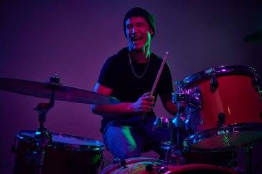 Neşeli, çağdaş davulcu pembe-mor sahne ışıklandırması ile gradyan stüdyo arka planına karşı çalıyor. Müzik ve sanat kavramı, hobi, konserler ve festivaller, modern kültür. Ad