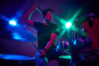 Pembe sahne ışıklandırmasında bagetleri olan enerjik davulcu gradyan stüdyo arka planına karşı. Müzik ve sanat kavramı, hobi, konserler ve festivaller, modern kültür. Ad