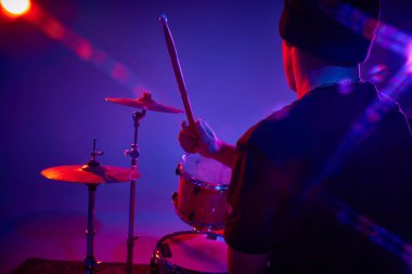 Pembe-mor sahne ışıklandırmasında sahne alan genç sanatsal bateristin arka plan portresi gradyan stüdyo arka planında. Müzik ve sanat kavramı, hobi, konserler ve festivaller, modern kültür. Ad