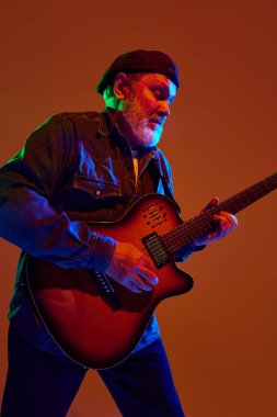 Kapüşonlu neşeli sakallı adam turuncu stüdyo arka planına karşı renkli neon ışıklı akustik gitar tıngırdatıyor. Müzik ve sanat kavramı, hobi, konserler ve festivaller, modern kültürün son sınıfları. Ad