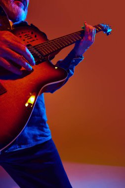 Olgun gitaristin renkli neon ışıklarıyla turuncu arka planda rock-balad akortları seslendirdiği kesilmiş bir fotoğraf. Müzik, sanat, konserler, festivaller, modern kültürdeki yaşlılar kavramı.