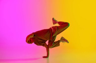 Modern dansçının dinamik fotoğrafı, neon ışıkta serbest dans ederken gradyan pembe-sarı arka planda. Hobi, spor, yaratıcılık, moda ve tarz, hareket, eylem kavramı. Ad