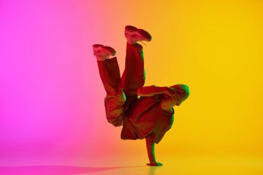 Artistik, genç adam, break-dansçı, neon ışıkta dans ediyor, gradyan pembe-sarı arka plana karşı. Hobi, spor, yaratıcılık, moda ve tarz, hareket, eylem kavramı. Ad