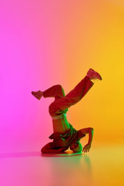 Havalı tavır genç adam, yetenekli serbest stil dansçı neon ışıkta dans ediyor gradyan pembe-sarı arka plana karşı. Hobi, spor, yaratıcılık, moda ve tarz, hareket, eylem kavramı. Ad