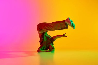 Sokak kıyafetleri giymiş genç dansçı, pembe-sarı arka plana karşı neon ışıkta serbest stil hareketler yapıyor. Sanat, hobi, spor, yaratıcılık, moda ve tarz, eylem kavramı. Ad