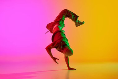 Genç adamın serbest stil performansının dinamik fotoğrafı, neon ışıkta, gradyan pembe-sarı arka plana doğru hareket ediyor. Sanat, hobi, spor, yaratıcılık, moda ve tarz, eylem kavramı. Ad