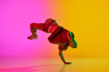 Serbest stilde dans eden genç bir adam. Eğitimler neon ışıklarıyla hareket ediyor. Gradyan pembe-sarı arka plana karşı. Sanat, hobi, spor, yaratıcılık, moda ve tarz, eylem kavramı. Ad