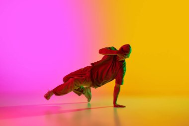 Havalı tavır genç adam hareket halinde neon ışıklarıyla gradyan pembe-sarı arka plana karşı break dans yapıyor. Sanat, hobi, spor, yaratıcılık, moda ve tarz, eylem kavramı. Ad
