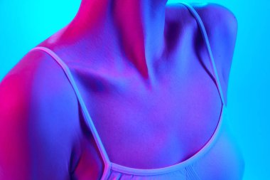 İyi korunmuş, pürüzsüz bir kadın vücudu, yakası, göğüsleri neon ışıkta, arka planda, spor sutyeninde. Güzellik ve sağlık kavramı, güneş koruması ve dinlenme için kozmetoloji ürünleri.
