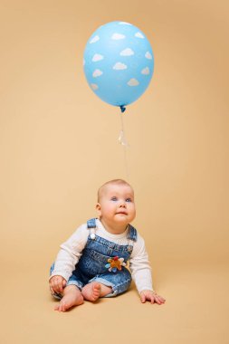 Genç kaşifin tasasız doğası. Kot pantolonlu bebek ve bej arka planda balonla rahat bir şekilde oturan sıcak süveter. Çocukluk kavramı, annelik, yaşam, doğum. İlan için alanı kopyala