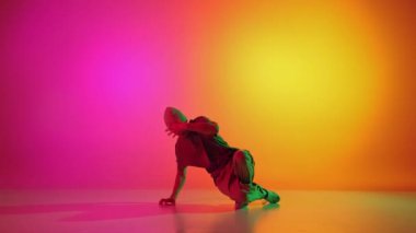 Genç, şık giyimli, parlak neon ışıkta dans eden bir adam gradyan pembe-sarı arka plana karşı. Breakdance. Hobi, spor, yaratıcılık, moda ve tarz, hareket, eylem kavramı. Ad