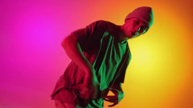 Sokak kıyafetleri giymiş yetenekli bir dansçı. Pembe-sarı arka plana karşı neon ışıkta serbest stil hareketleri yapıyor. Sanat, hobi, spor, yaratıcılık, moda ve tarz, eylem kavramı. Ad