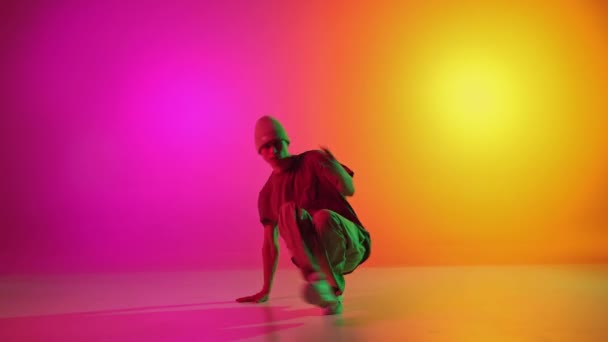 若い男 才能のあるブレイクダンサーは グラデーションピンクイエローの背景に対して混合されたネオンライトで動きながら踊ります スポーツ 創造性 ファッション スタイル モーション アクションの概念 アドベンチャー — ストック動画