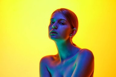 Çekici, çıplak omuzlu genç bir kadının portresi. Stüdyonun arka planında, neon ışıkta kameraya bakıyor. Doğal güzellik kavramı, organik kozmetik, spa prosedürleri, yüz bakımı.