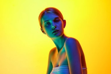 Tepedeki çekici genç kadın karışık neon ışıkta kameraya kendinden emin bakıyor. Gradyan stüdyo arka planına karşı. Doğal güzellik kavramı, organik kozmetik, spa prosedürleri, yüz bakımı.