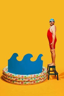 Mayo giymiş bir adam, sarı stüdyo arka planına karşı soyut suyla çocuk havuzuna dalmaya hazırlanıyor. Pop sanatı, spor, eğitim, rekabet, hobi, aktivite kavramı.