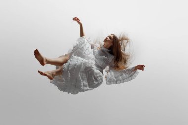 Zarif beyaz elbiseli, ince fırfırlı genç bir kadın, beyaz stüdyo arka planına doğru yükseliyor gibi görünüyor. Güzellik kavramı, kadınsı zarafet ve saflık, rüya ve gerçeklik..