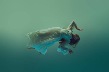 Derin sularda zahmetsizce süzülen beyaz elbiseli bir kadın. Model, dingin su arka planına karşı havalanır. Güzellik kavramı, zarafet, gizem ve derinlik, ağırlıksızlık. Ad