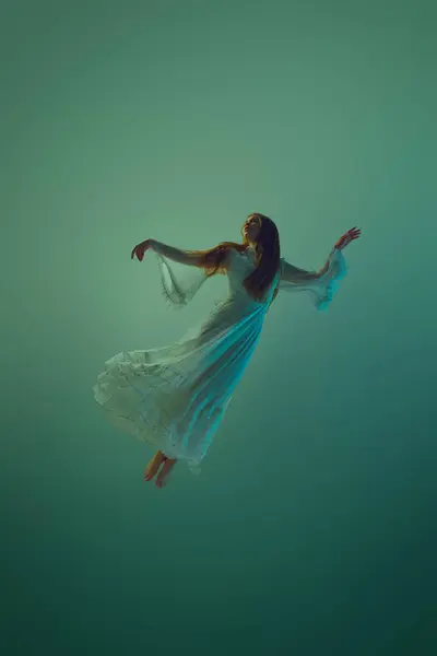 Young elegant woman dressed in white gown dancing or descent through water against serene aqua background. Concept of underwater fantasy, freedom and weightlessness, mystery and depth. Ad